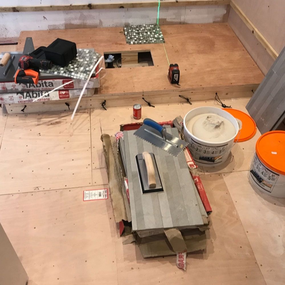 Workman's tools and tiles laid out on kitchen floor ready for screeding and installation